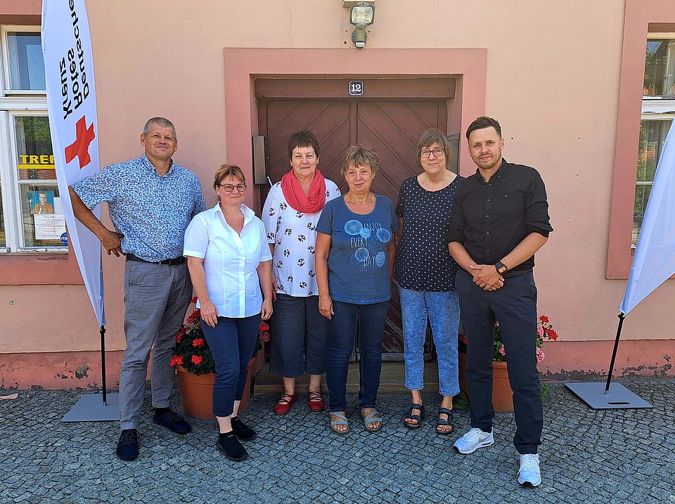 Der Beeskower Kämmerer Steffen Schulze, die Leiterin der DRK-Geschäftsstelle Eisenhüttenstadt, Daniela Koch, Marion Brunnert von der Landesarbeitsgemeinschaft der Selbsthilfekontaktstellen Brandenburg e.V., Helfer*innenkreis-Koordinatorin Cornelia Ewert, Ramona Weinert von der Selbsthilfe-Kontaktstelle und der Beeskower Bürgermeister Robert Czaplinski (v. l.) vor dem neuen Sitz von Selbsthilfe-Kontaktstelle und Helfer*innenkreis in der Breitscheidstraße 12